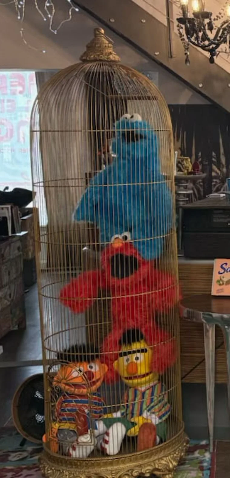 Vergoldeter Vogelkäfig mit drei Stoffpuppen