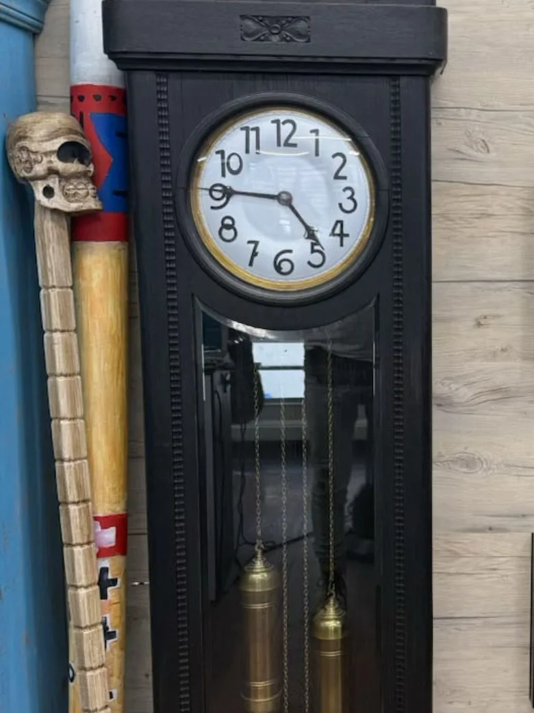 Alte Standuhr neben bemalten Stäben mit Schädelgriff